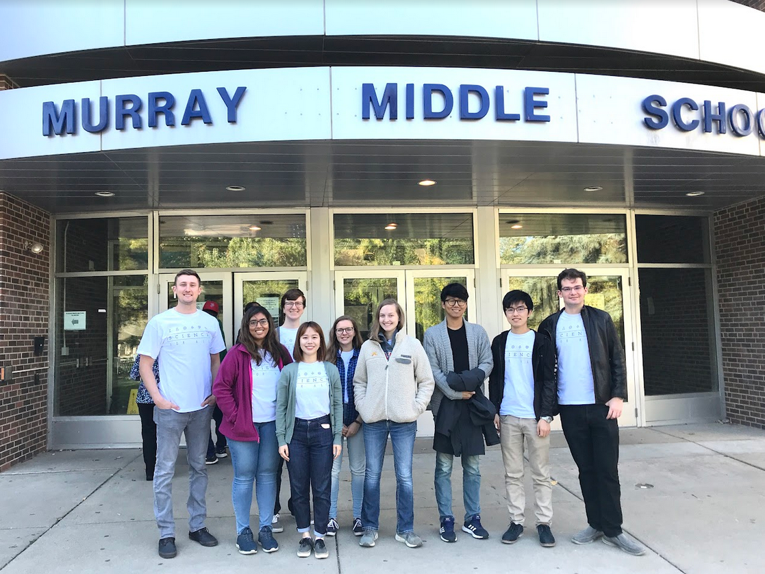 A group of SFA volunteers stands outside Murray Middle School, with the name of the school in bold, blue text. 