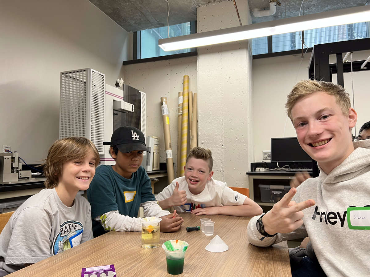 A group of students smile with their fiters and beakers with colorful fluid. 