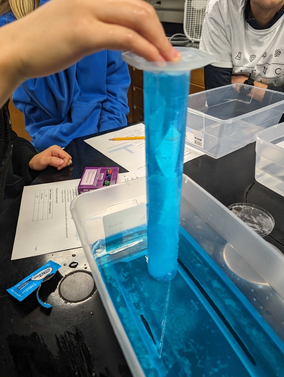 An inverted graduated cylinder filled with blue liquid used to measure carbon dioxide displacement.