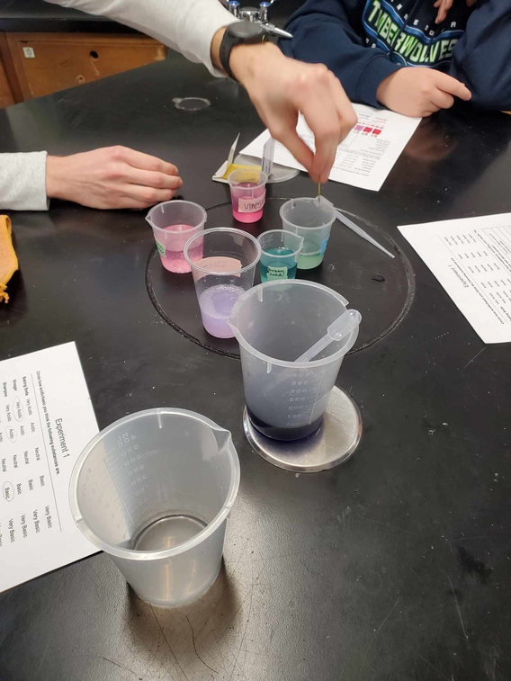 Beakers filled with colorful liquids (bright pink, teal, and purple) to represent a range of materials with different pH.